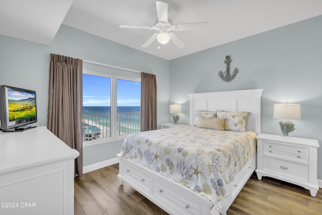 bedroom featuring a water view, hardwood / wood-style floors, and ceiling fan