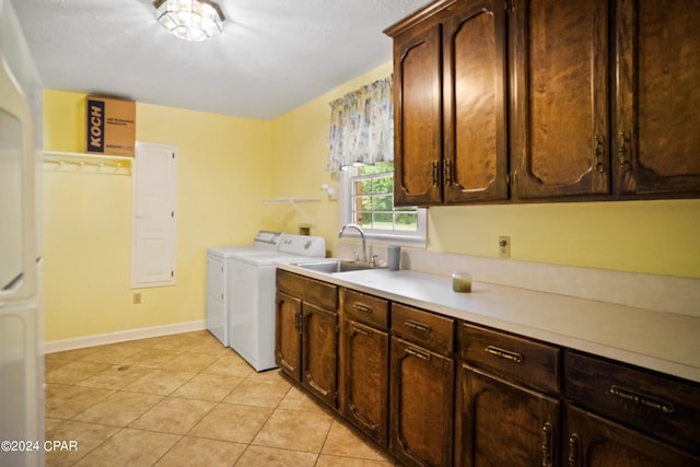 clothes washing area featuring sink, washing machine and dryer, light tile flooring, and cabinets