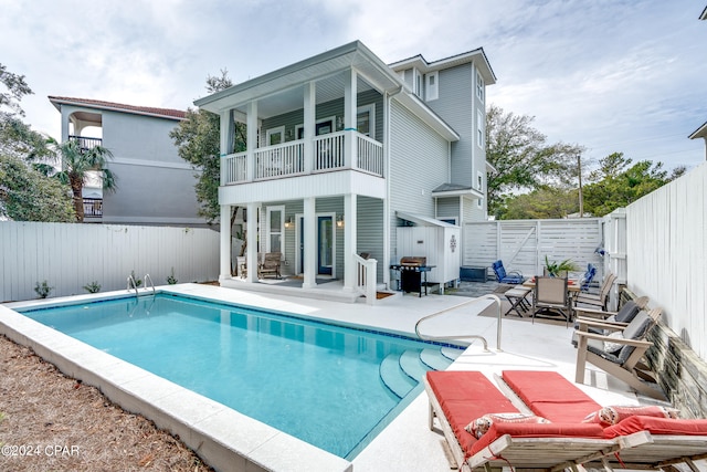 rear view of house featuring a patio, a fenced in pool, and a balcony