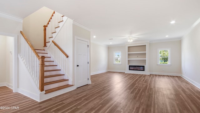 unfurnished living room with ceiling fan, ornamental molding, built in shelves, and dark wood-type flooring