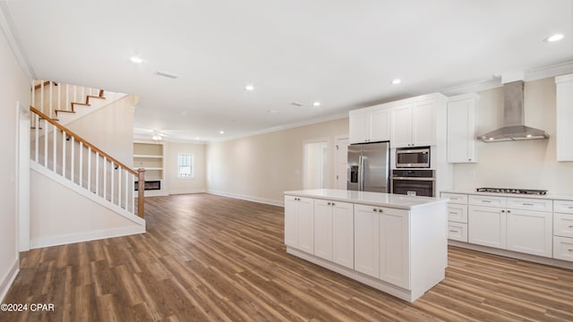 kitchen with appliances with stainless steel finishes, white cabinets, wood-type flooring, and wall chimney exhaust hood