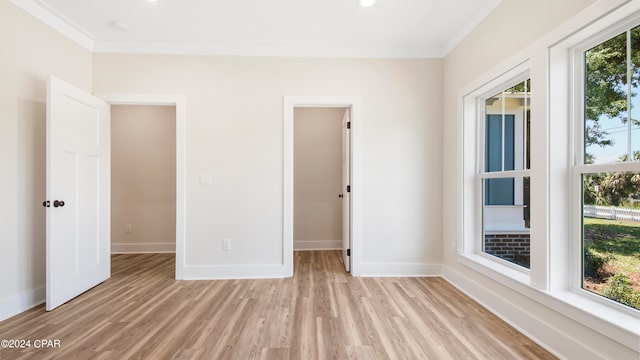 unfurnished bedroom featuring a spacious closet, crown molding, a closet, and light wood-type flooring