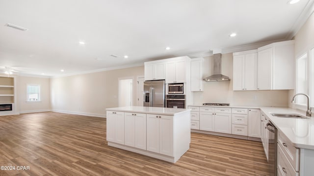 kitchen with stainless steel appliances, light wood-type flooring, a kitchen island, wall chimney range hood, and sink