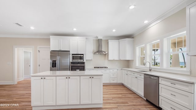 kitchen featuring wall chimney range hood, sink, light wood-type flooring, and stainless steel appliances