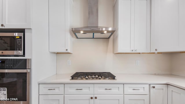 kitchen featuring wall chimney range hood, white cabinetry, and appliances with stainless steel finishes