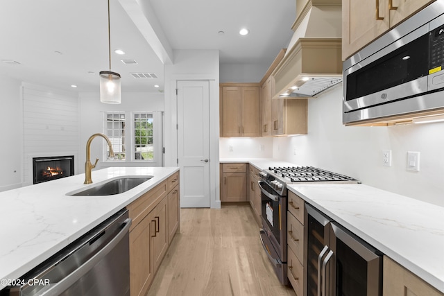 kitchen featuring appliances with stainless steel finishes, a fireplace, sink, light hardwood / wood-style flooring, and custom range hood