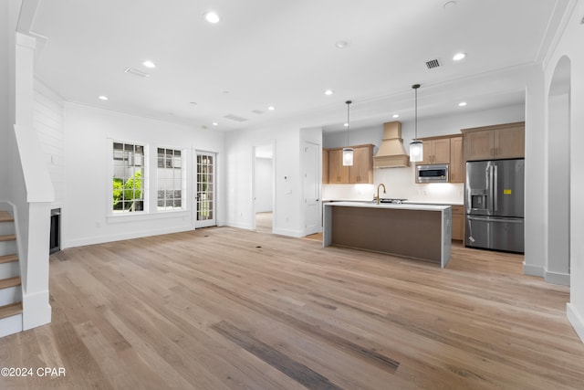 kitchen featuring custom exhaust hood, light wood-type flooring, hanging light fixtures, stainless steel appliances, and a center island with sink