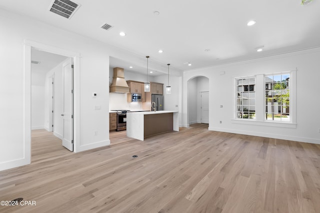 kitchen featuring premium range hood, decorative light fixtures, appliances with stainless steel finishes, a center island with sink, and light hardwood / wood-style floors