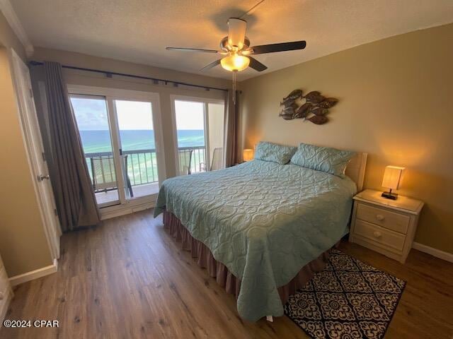 bedroom with hardwood / wood-style floors, ceiling fan, a water view, and access to exterior