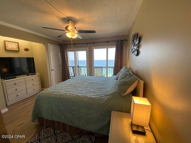 bedroom with a water view, ceiling fan, access to exterior, a textured ceiling, and light wood-type flooring