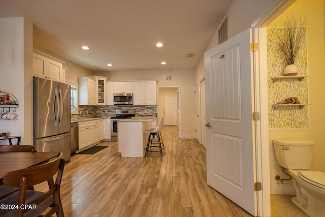 kitchen featuring white cabinetry, a center island, light hardwood / wood-style flooring, a kitchen bar, and appliances with stainless steel finishes