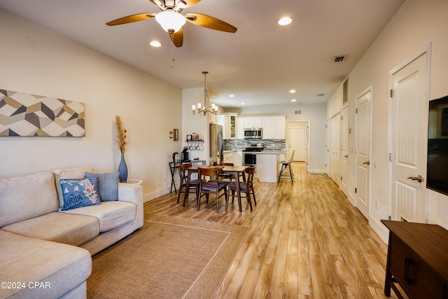 living room featuring ceiling fan with notable chandelier and light hardwood / wood-style floors