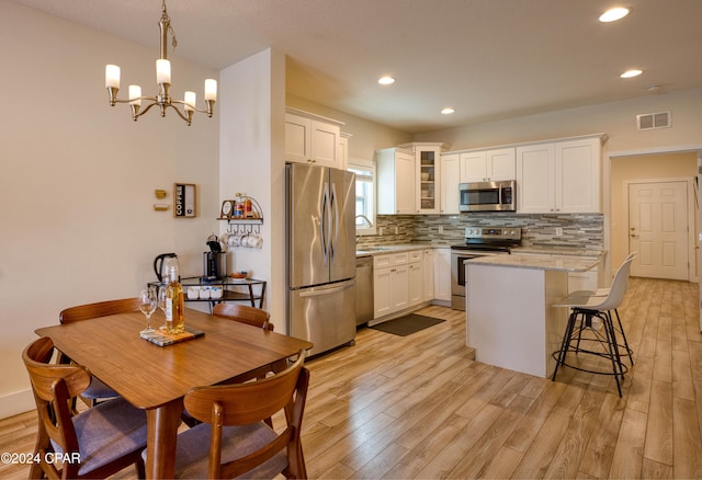 kitchen featuring white cabinets, decorative light fixtures, light wood-type flooring, and stainless steel appliances