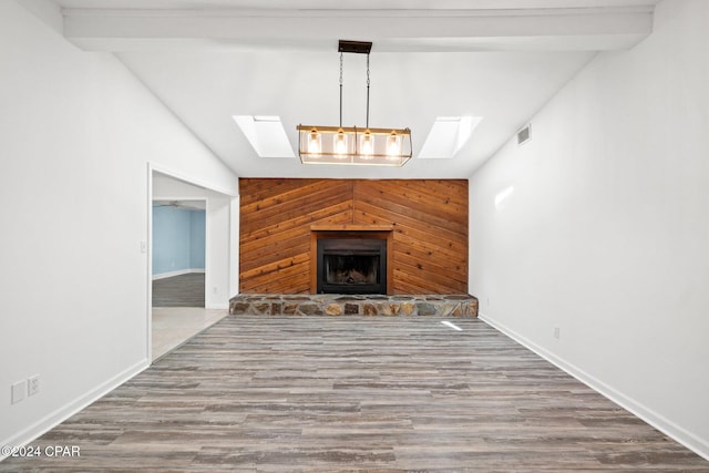 unfurnished living room featuring lofted ceiling with skylight, wooden walls, wood-type flooring, and a fireplace