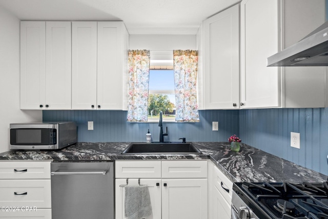 kitchen with appliances with stainless steel finishes, sink, white cabinetry, dark stone counters, and range hood