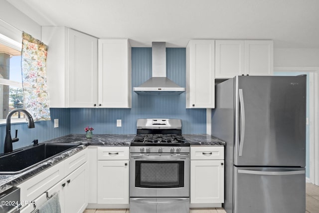 kitchen featuring appliances with stainless steel finishes, sink, wall chimney exhaust hood, white cabinets, and dark stone countertops