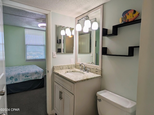 ensuite bathroom featuring a textured ceiling, toilet, connected bathroom, and vanity