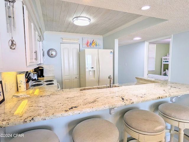 kitchen with white fridge with ice dispenser, ornamental molding, wooden ceiling, and light stone counters