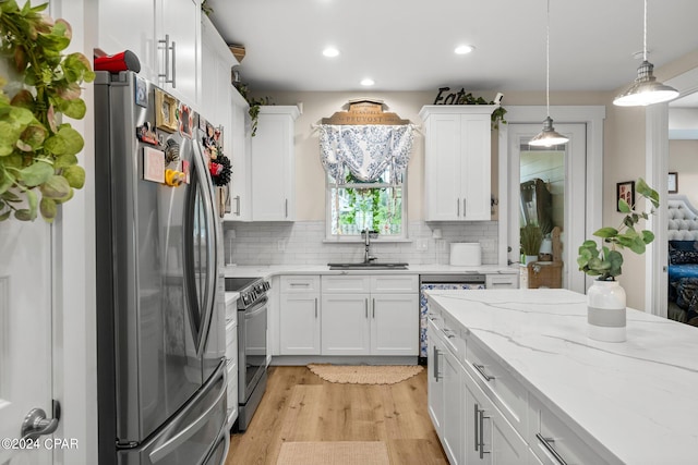 kitchen with decorative light fixtures, white cabinetry, backsplash, appliances with stainless steel finishes, and light hardwood / wood-style floors