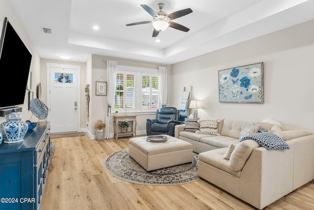 living room with a tray ceiling, ceiling fan, and light hardwood / wood-style floors