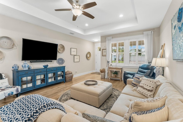 living room featuring light hardwood / wood-style floors, ceiling fan, and a tray ceiling