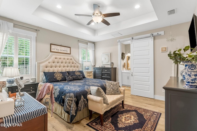 bedroom featuring connected bathroom, multiple windows, a raised ceiling, and a barn door