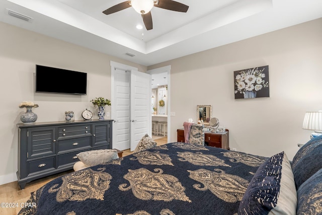 bedroom with light hardwood / wood-style flooring, ceiling fan, ensuite bath, and a tray ceiling