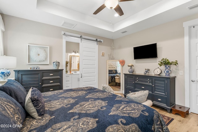 bedroom with a raised ceiling, light hardwood / wood-style floors, ensuite bathroom, and a barn door