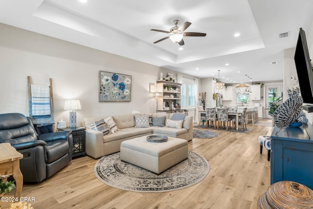 living room featuring light hardwood / wood-style floors, ceiling fan, and a raised ceiling