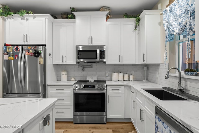 kitchen featuring appliances with stainless steel finishes, light hardwood / wood-style flooring, white cabinets, and light stone counters