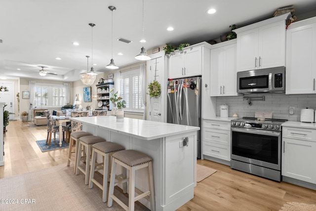 kitchen with decorative light fixtures, appliances with stainless steel finishes, ceiling fan, and light hardwood / wood-style flooring