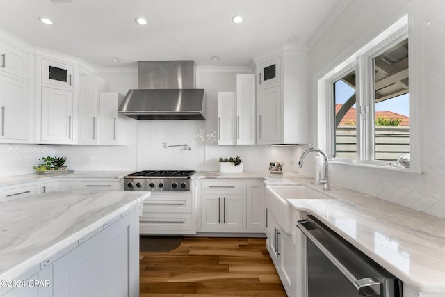 kitchen featuring stainless steel dishwasher, wood-type flooring, backsplash, wall chimney range hood, and white cabinets