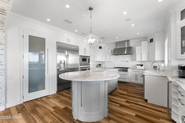 kitchen with hardwood / wood-style floors, wall chimney exhaust hood, stainless steel appliances, and a center island with sink