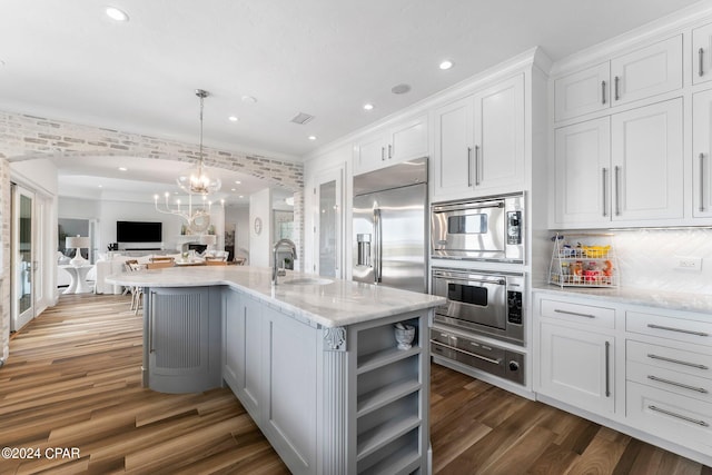 kitchen featuring hardwood / wood-style floors, an island with sink, built in appliances, pendant lighting, and white cabinetry