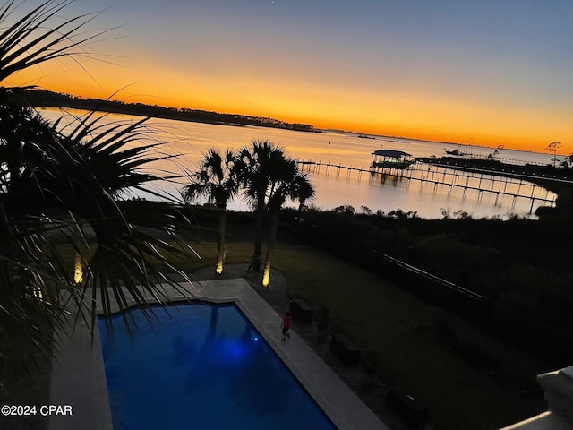 pool at dusk with a water view and a dock