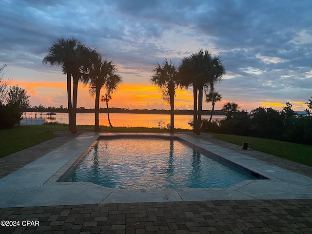 pool at dusk featuring a patio and a water view