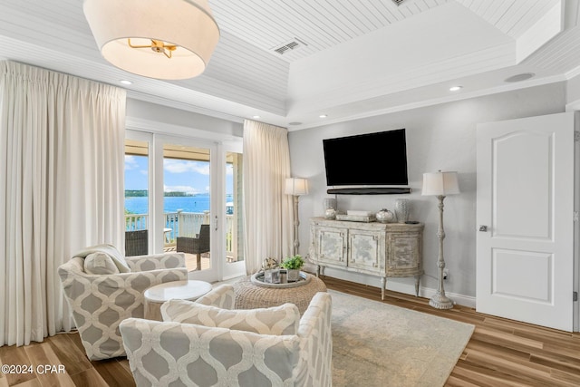 living room with a tray ceiling, a water view, and hardwood / wood-style floors