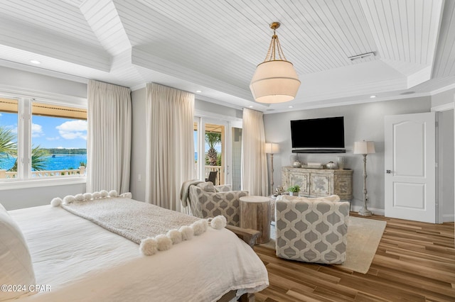 bedroom with multiple windows, a tray ceiling, a water view, and wood-type flooring