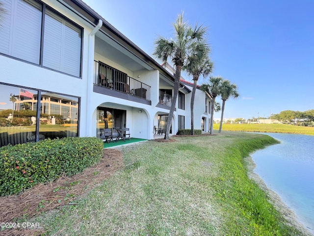 back of house with a water view, a yard, and stucco siding