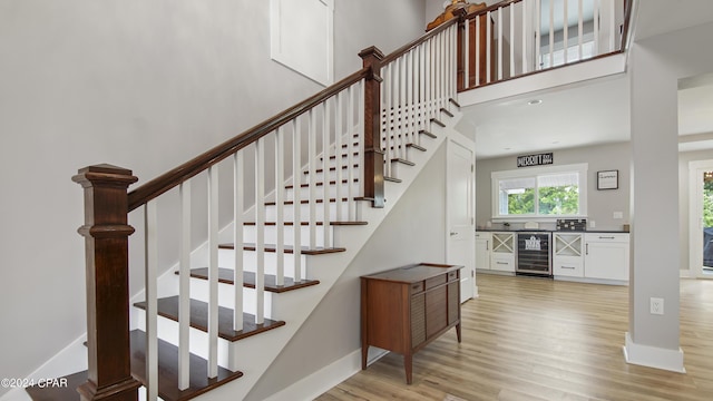 staircase featuring a towering ceiling, wood-type flooring, and beverage cooler