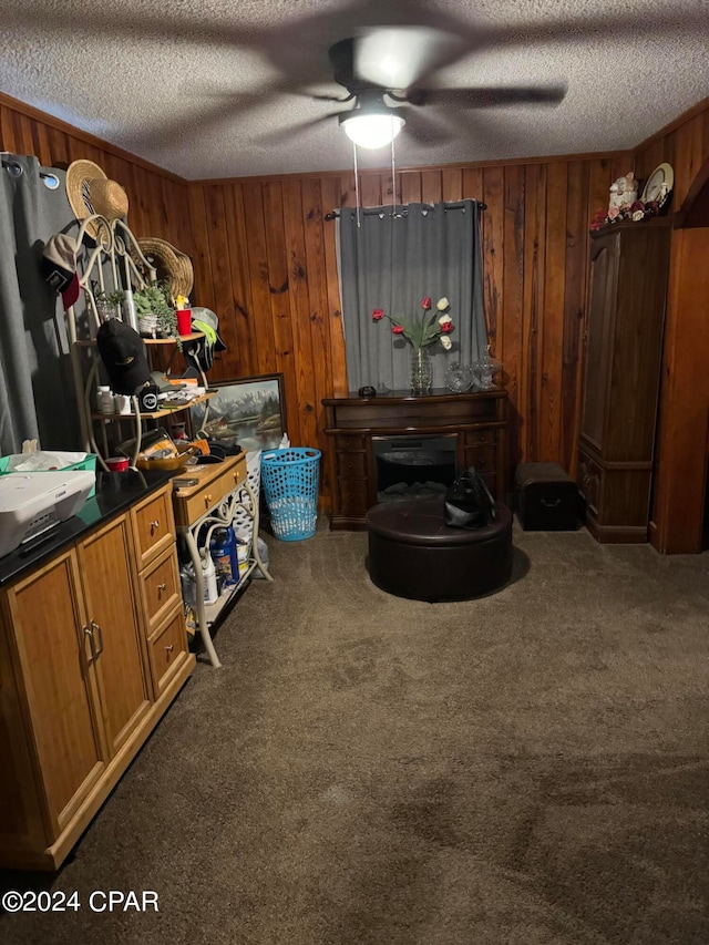 misc room with wooden walls, dark colored carpet, a textured ceiling, and ceiling fan