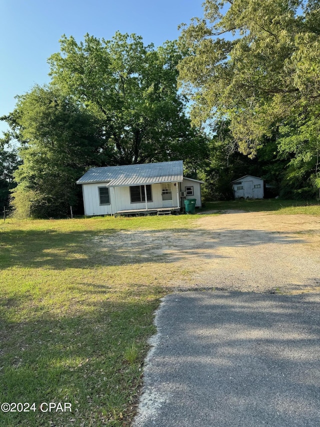 view of front of house featuring metal roof, covered porch, an outdoor structure, driveway, and a front yard