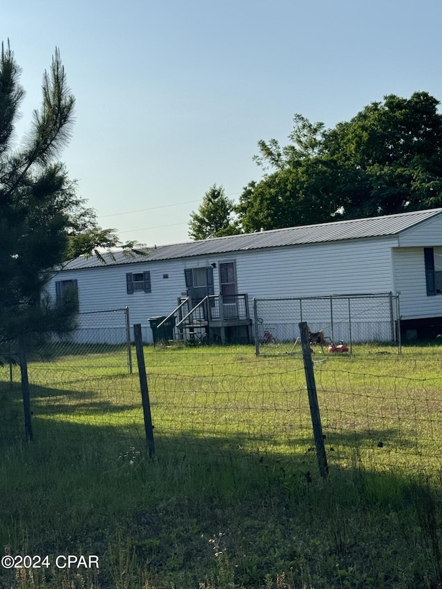 back of house with metal roof, a lawn, and fence