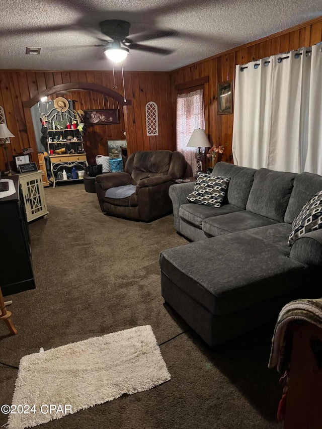 carpeted living room featuring wooden walls, a textured ceiling, and ceiling fan