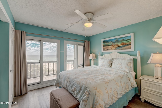 bedroom with hardwood / wood-style floors, ceiling fan, a water view, and access to exterior