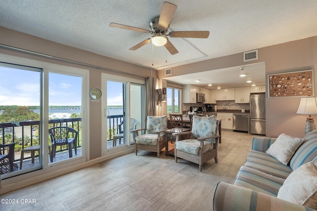 living room featuring ceiling fan, a healthy amount of sunlight, light hardwood / wood-style flooring, and a textured ceiling