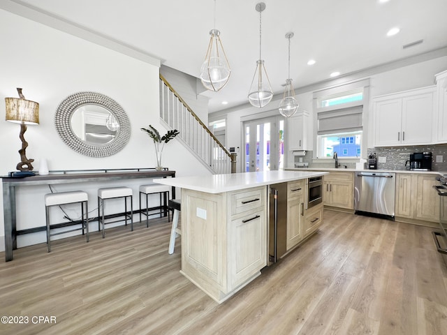 kitchen with a kitchen island, light wood-type flooring, appliances with stainless steel finishes, decorative light fixtures, and a breakfast bar