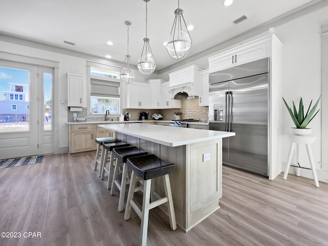 kitchen featuring white cabinetry, high end appliances, backsplash, a center island, and light wood-type flooring