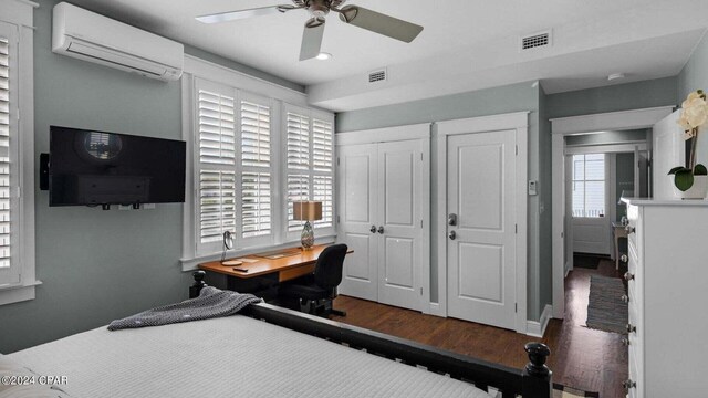 bedroom with ceiling fan, a wall mounted air conditioner, dark hardwood / wood-style flooring, and two closets