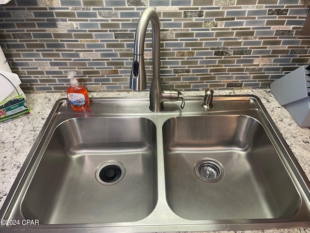 interior details with tasteful backsplash, light stone countertops, and sink